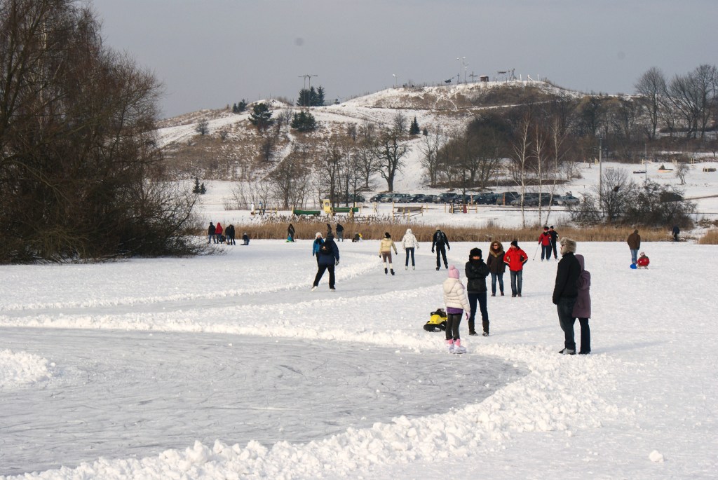 Łyżwiarze na zamarzniętym jeziorku w Myślęcinku. W tle stok narciarski